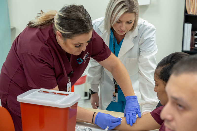 Instructor looking on as a nursing student prepares to practice injection on another student